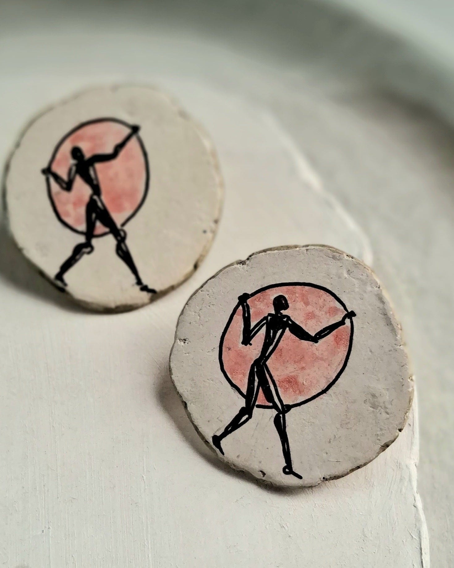 Round ceramic pieces with black silhouette and pink circle design on a white surface