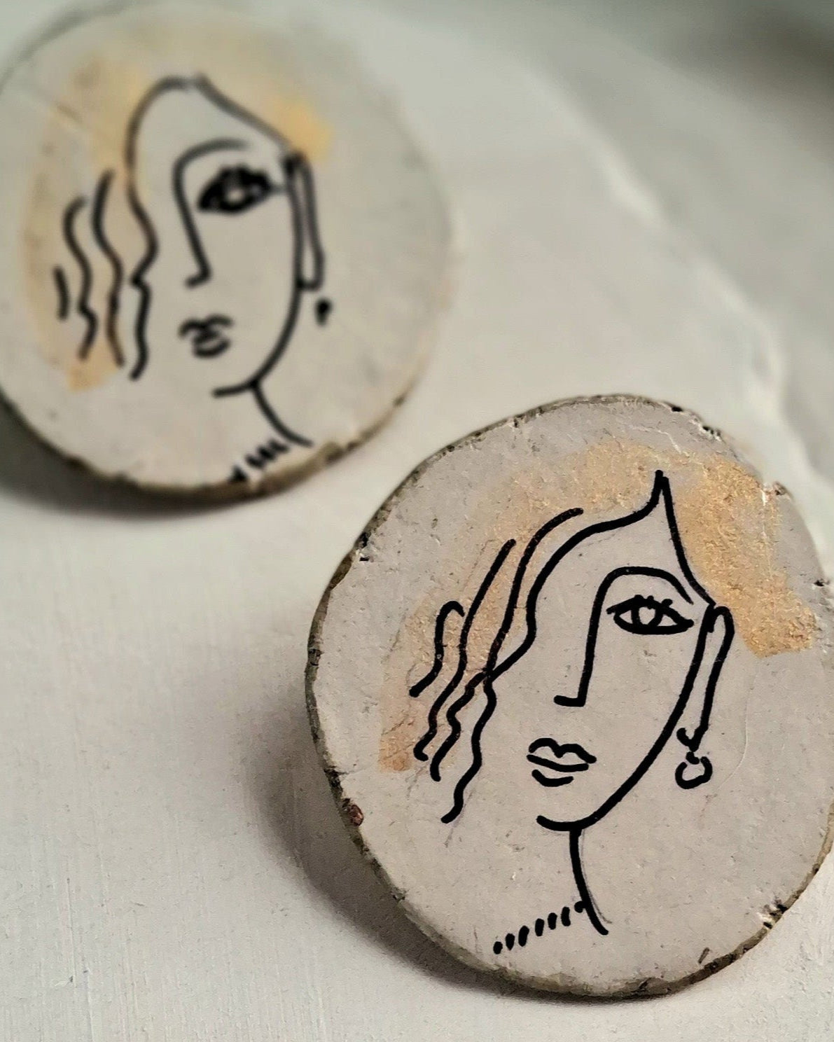 Two circular ceramic pieces with abstract face designs on a light background