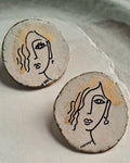Ceramic earrings with face designs on a textured surface
