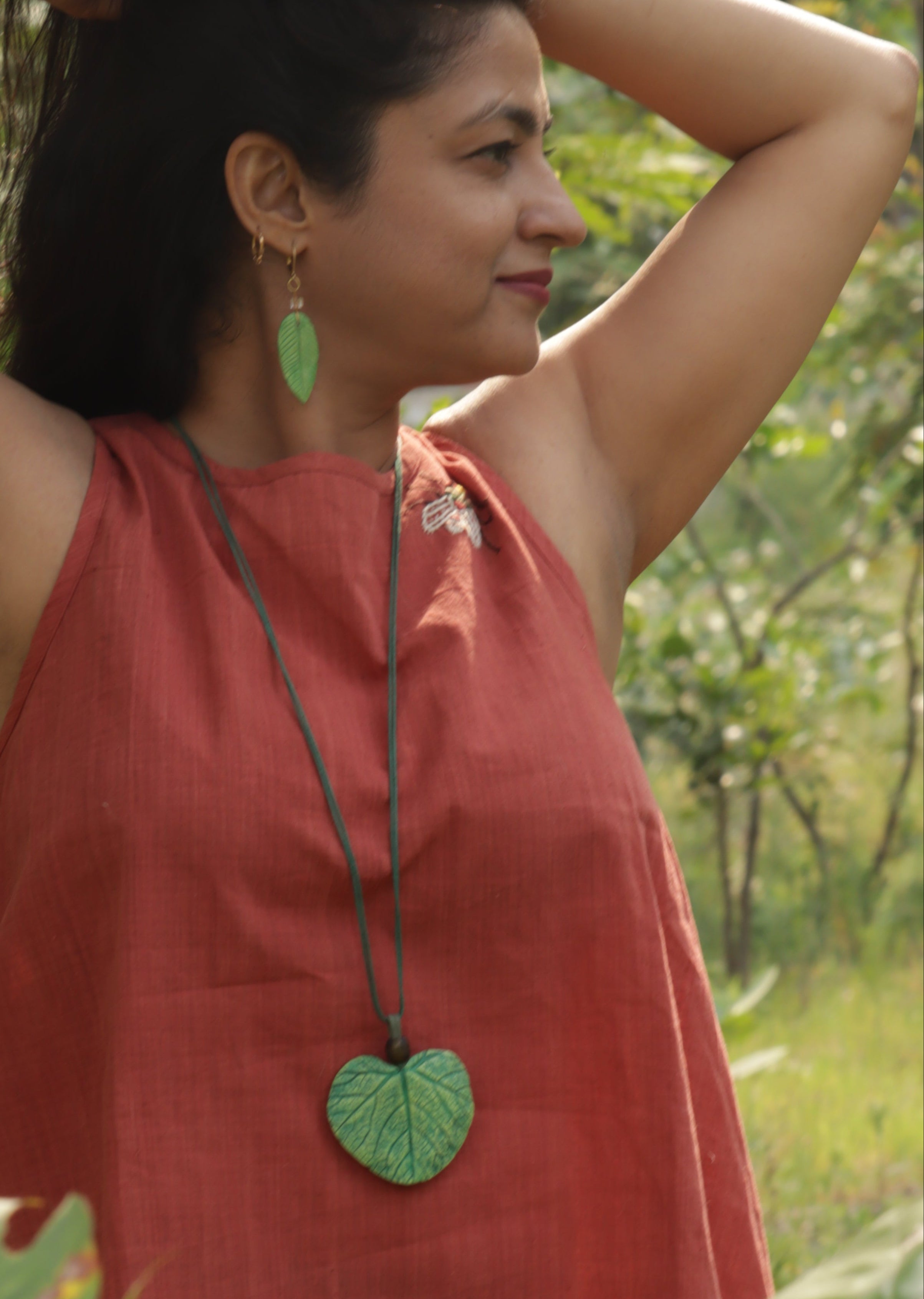 Woman in a red dress with green heart-shaped earrings standing among trees