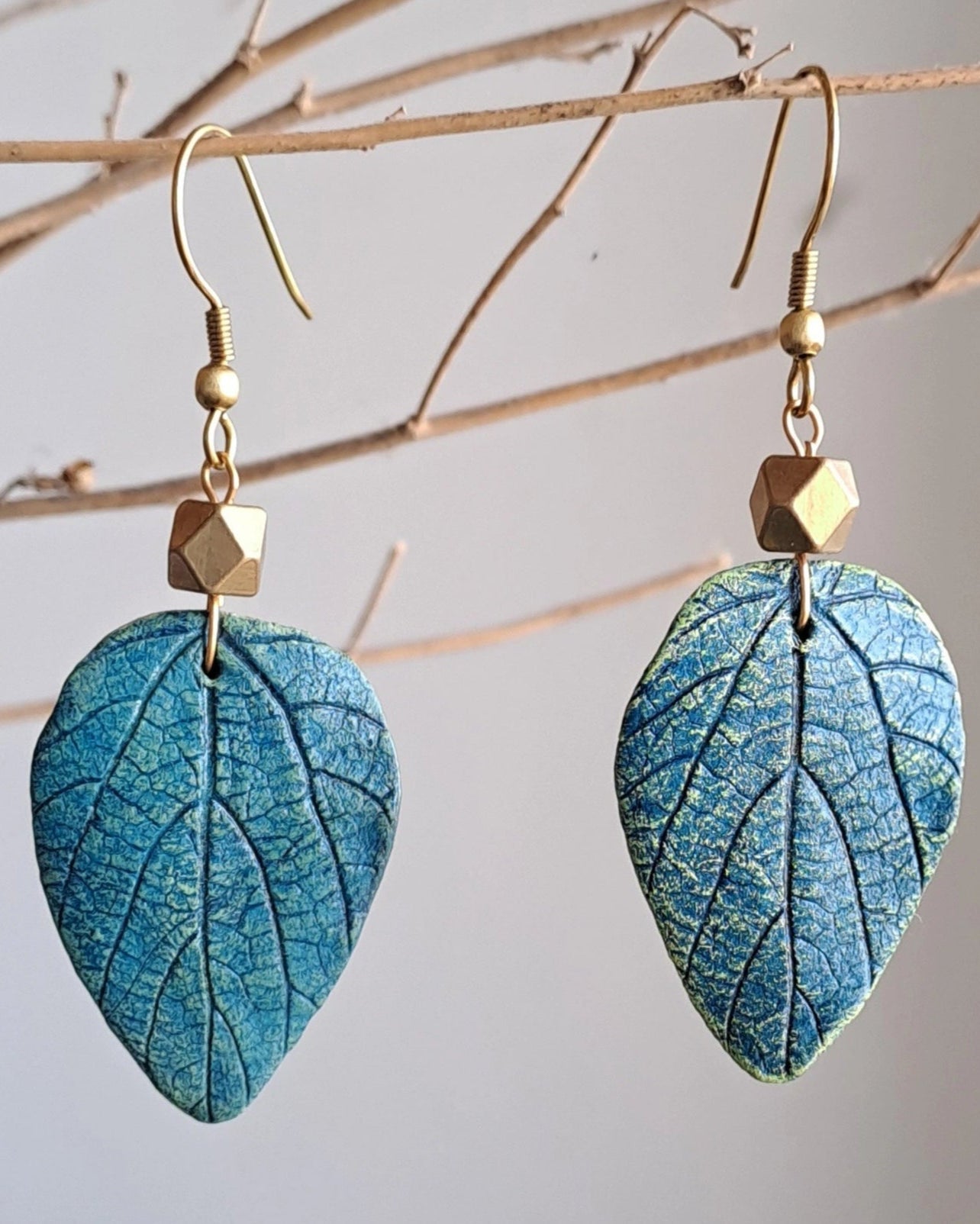 Blue leaf-shaped earrings with gold hooks on a branch background