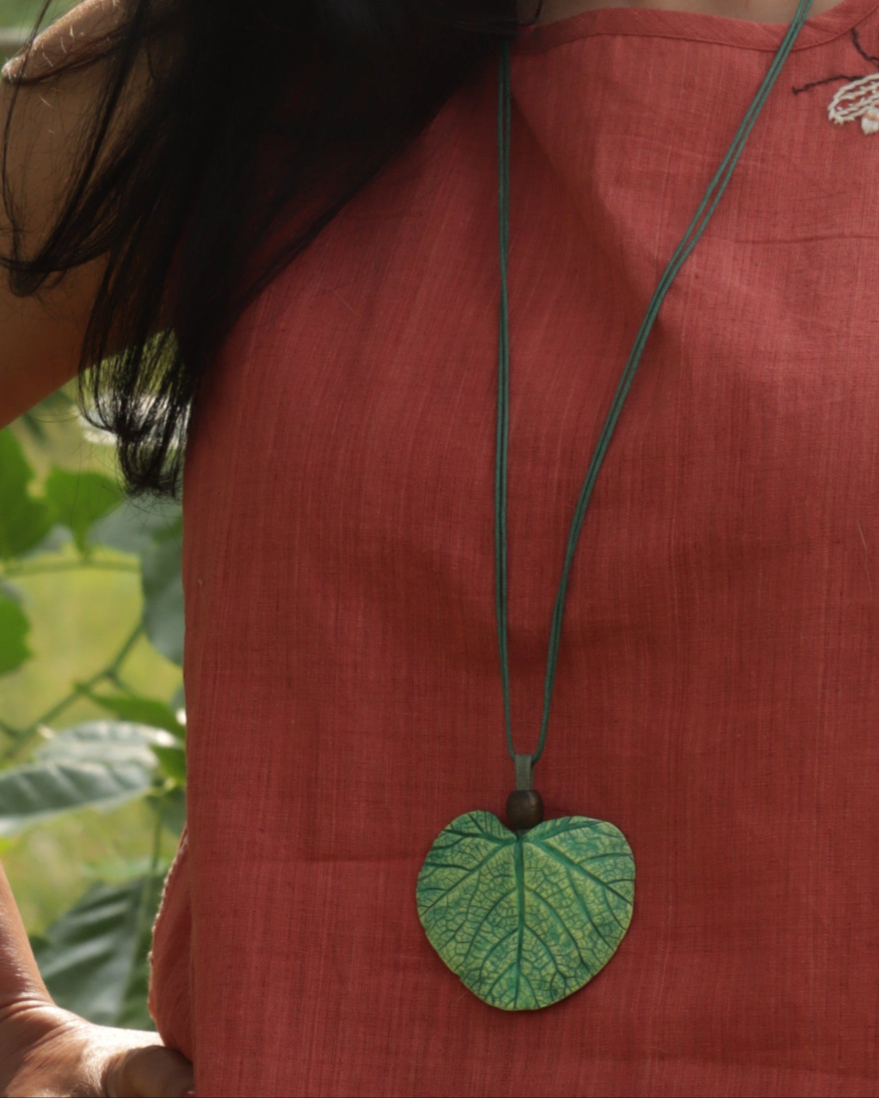 Person wearing a red garment with a green leaf-shaped pendant on a necklace.