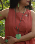 Woman wearing a red sleeveless top with a green leaf pendant necklace and earrings outdoors.